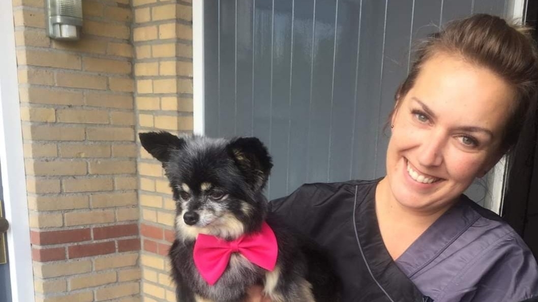 De trimster van The Generation's lacht bij de deur van de salon met een klein zwart hondje met een roze strikje op de arm